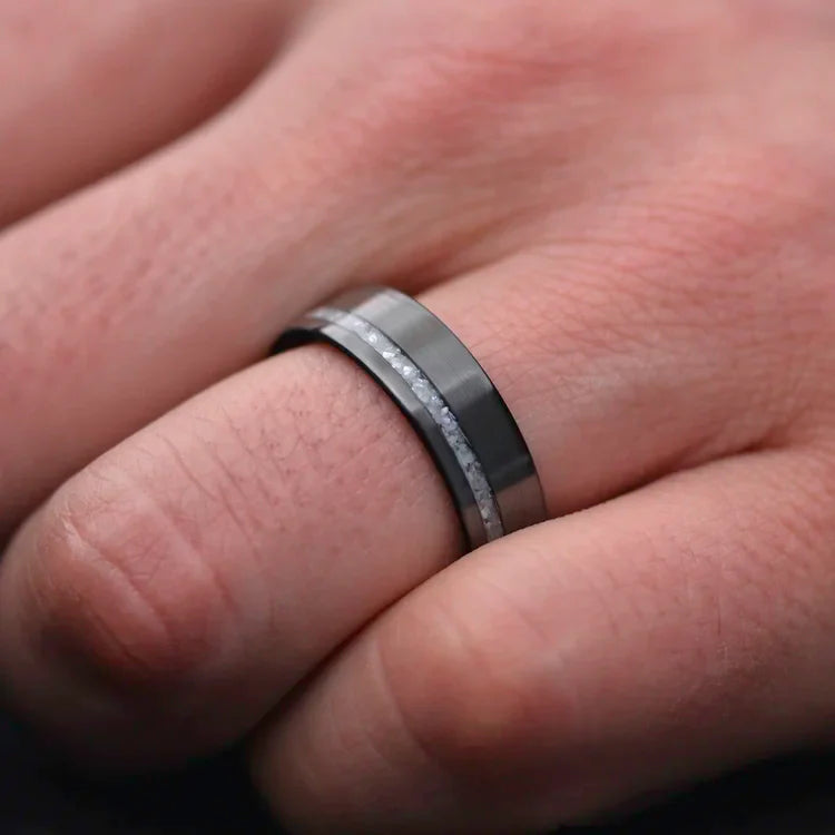 Black titanium wedding band with pearl inlay on a hand, featuring a polished flat profile, 7mm width, and free engraving for a unique mens wedding ring.