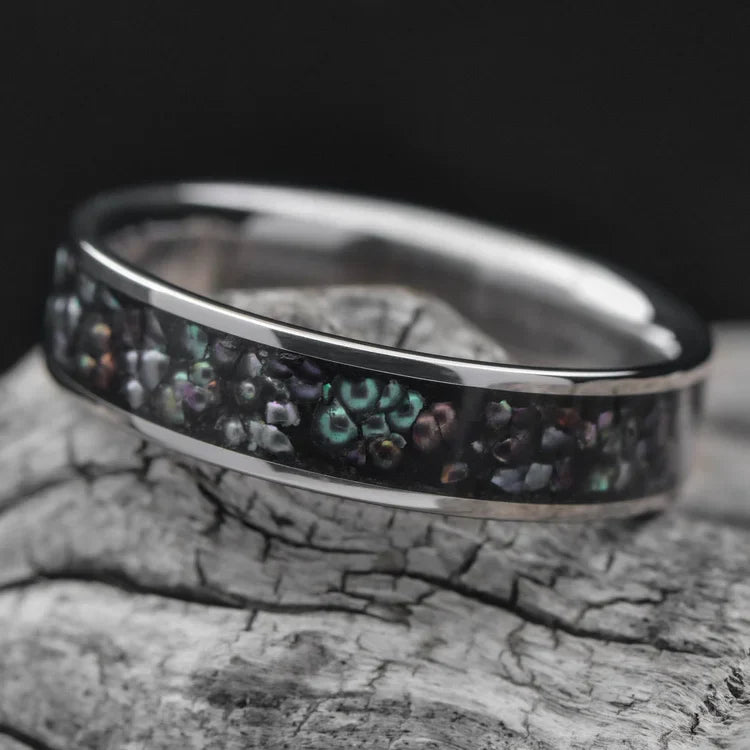 Titanium wedding band with central black pearl inlay, 6mm mens ring, polished flat profile, displayed on a white sea branch, free engraving available.