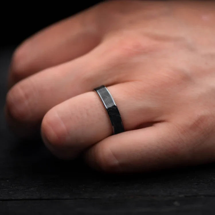Black titanium wedding band with central forged inlay on hand, featuring free engraving, 5mm width, simple custom ring with polished flat profile.