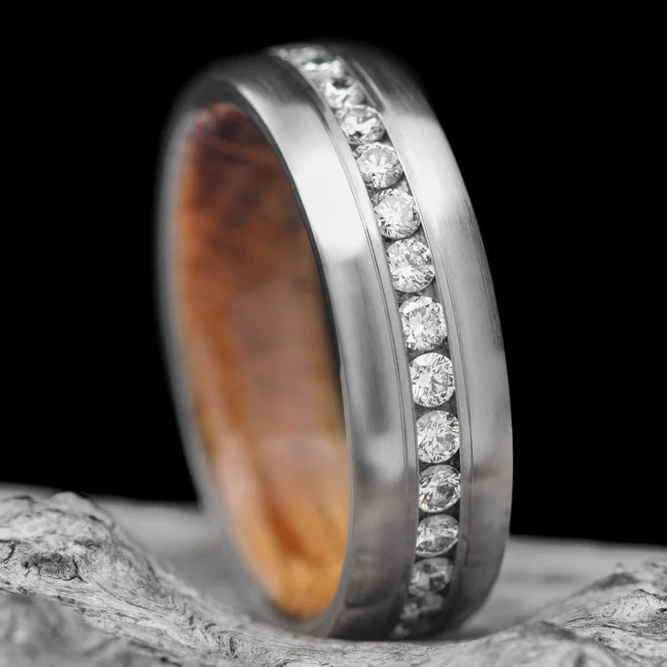 Brushed titanium wedding band with whiskey barrel oak inner sleeve, featuring eternity set stones, 7mm mens ring, displayed on a white sea branch, free engraving available.