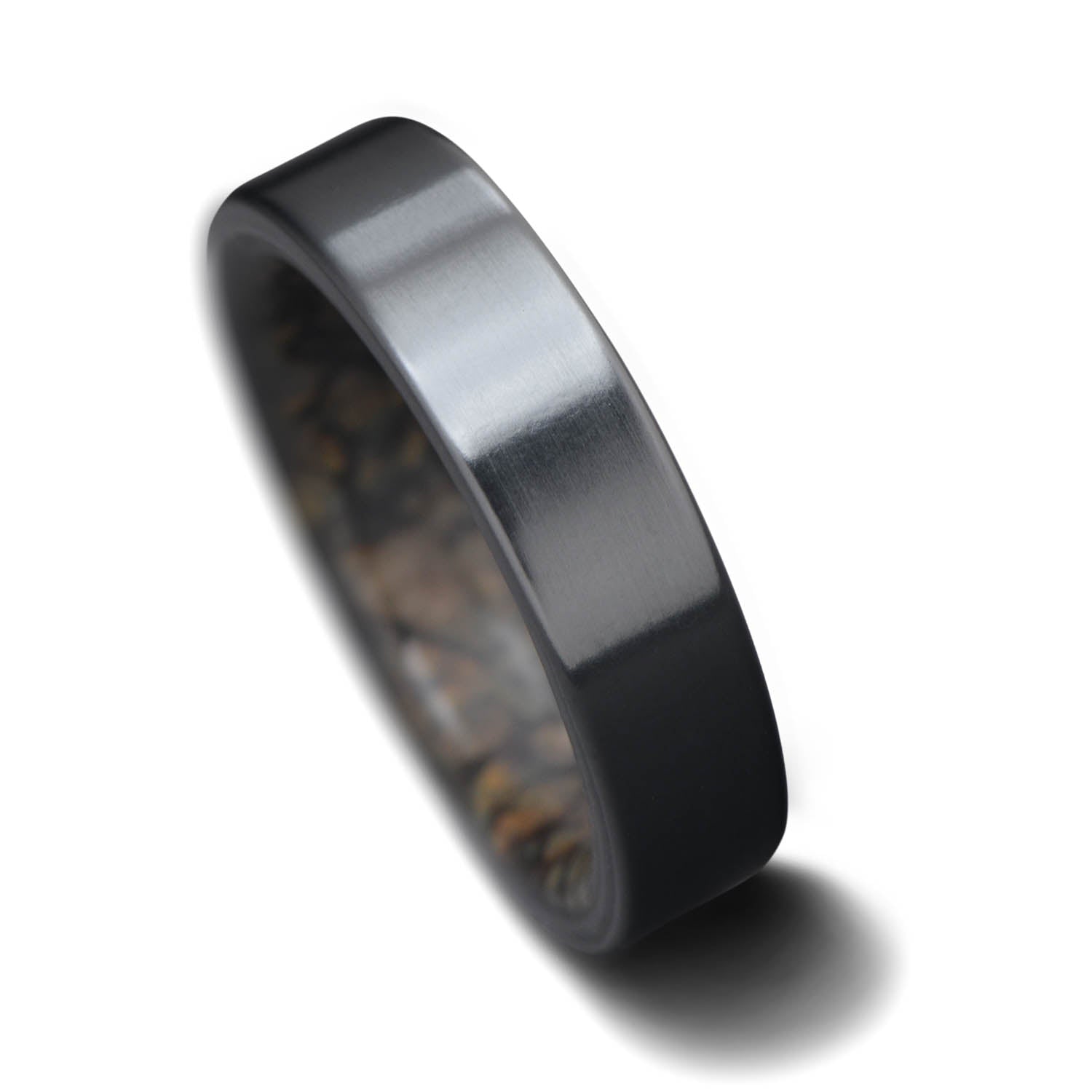 Black titanium wedding ring with dinosaur bone inner sleeve, 5mm width, custom engraving available, unique simple design, displayed on a white sea branch.