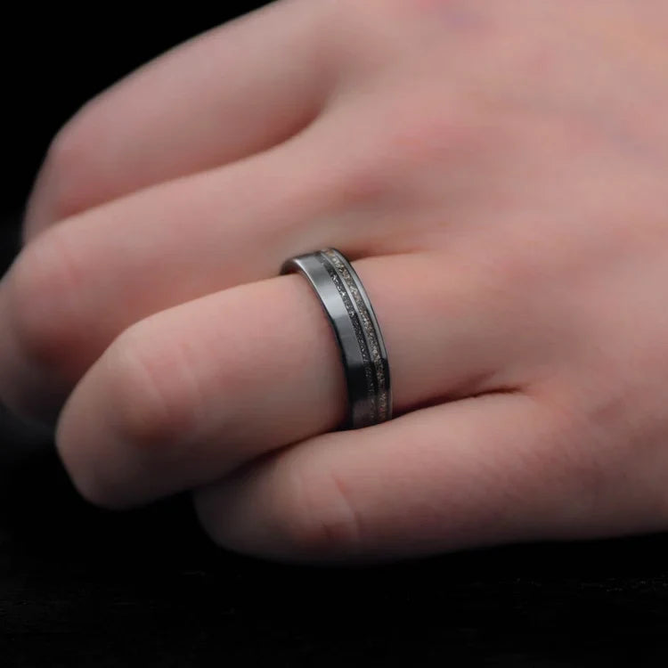 Mens black titanium wedding band with meteorite and crushed T-Rex inlays, 6mm matte flat profile, unique design, free engraving, worn on a hand.