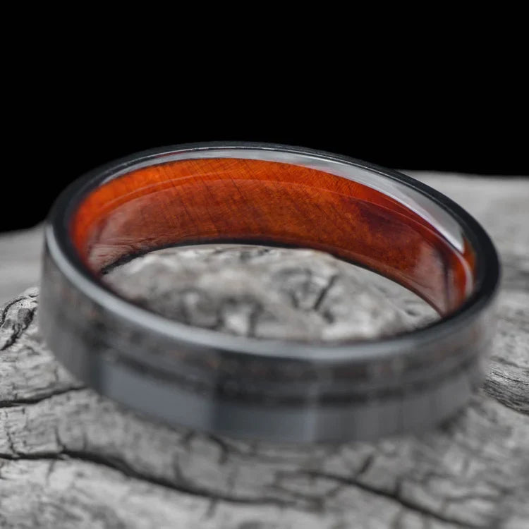 Black titanium wedding band with meteorite and crushed T-Rex inlays, 6mm mens matte flat profile ring, unique mens ring, displayed on a white sea branch, free engraving available.