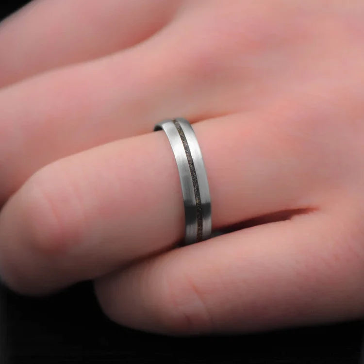 Titanium wedding band with central crushed T-Rex inlay on a hand, featuring free engraving, 5mm width, simple custom design, unique wedding band.