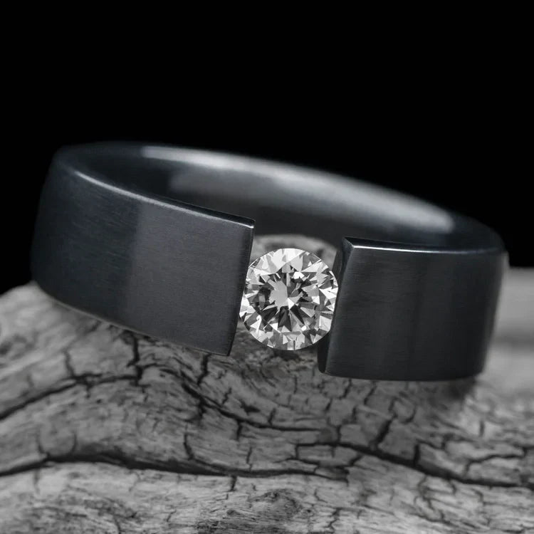 Black titanium wedding band with tension set diamond, featuring free engraving, 7mm width, mens wedding ring with brushed flat profile, displayed on a white sea branch.