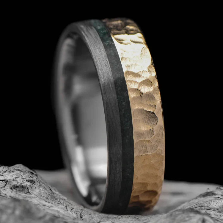 14K yellow gold mens wedding band with unidirectional and moss agate inlays, 7mm hammered flat profile, unique design, free engraving, displayed on a white sea branch.