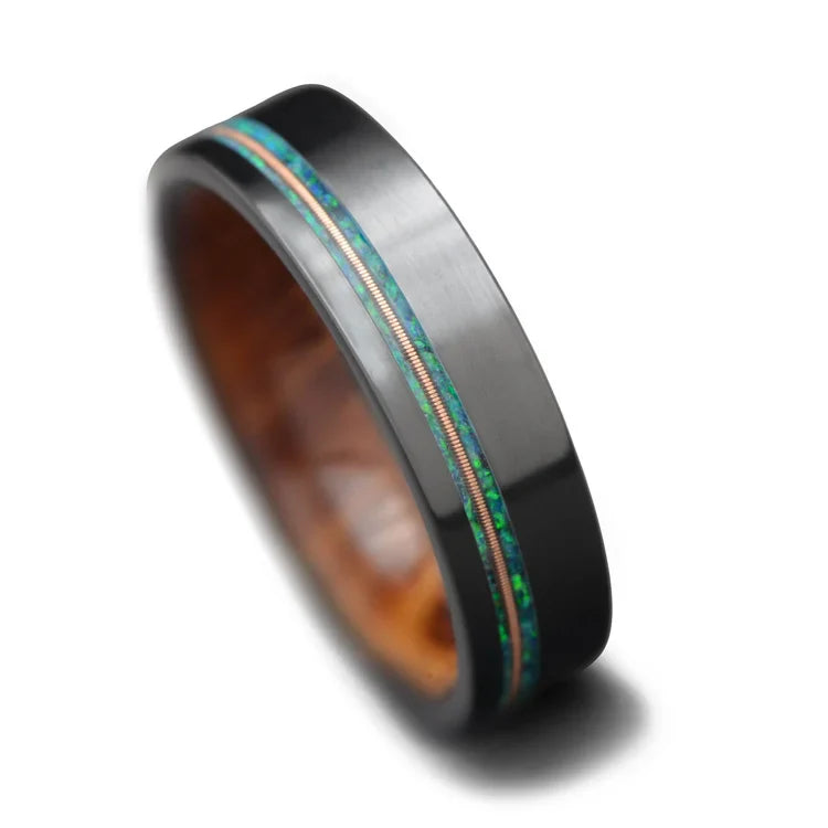 Black titanium wedding band with blue opal and guitar string inlay, featuring a whiskey barrel oak inner sleeve, 6mm mens ring, free engraving available, displayed on a white background.