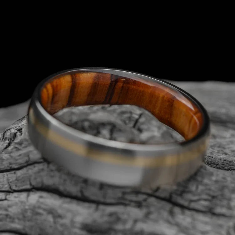 Titanium wedding band with 10KY gold and olivewood inlay, featuring a unique brushed domed profile, displayed on a white sea branch, 6mm mens ring with free engraving.