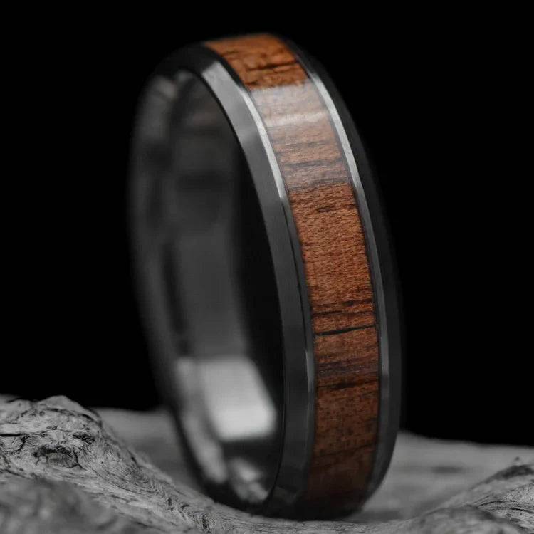 Black titanium wedding band with central walnut inlay, 6mm mens ring, brushed bevel profile, free engraving, displayed on white sea branch.
