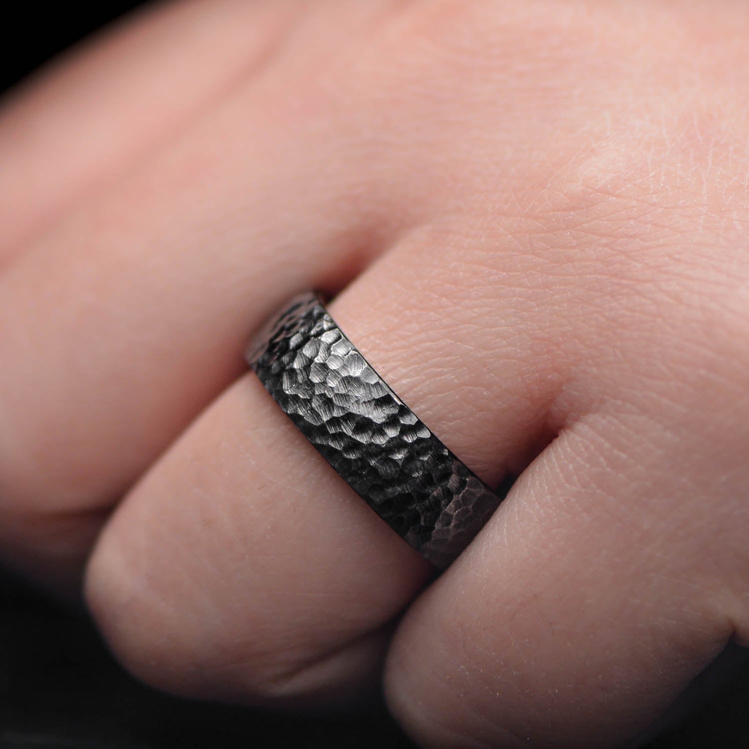 Black titanium wedding band with whiskey barrel oak inner sleeve, featuring a hammered domed design, 7mm mens ring, displayed on a white sea branch, offering free engraving, unique mens wedding band.