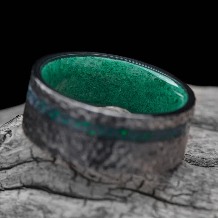 Black titanium wedding band with black emerald opal and malachite inlays, 9mm mens hammered flat profile ring, displayed on a white sea branch, free engraving available.