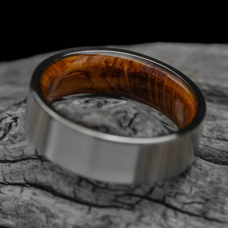 Titanium wedding band with whiskey barrel oak inner sleeve, 7mm mens ring, brushed flat profile, free engraving, displayed on a white sea branch.