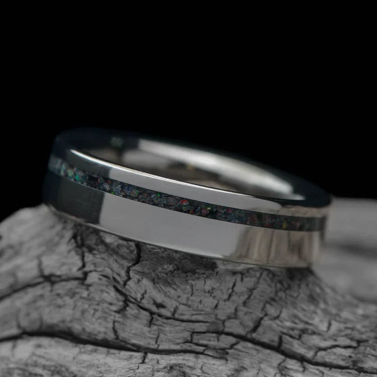 Titanium wedding band with black fire opal inlay, 5mm polished flat profile, custom simple ring with free engraving, displayed on a white sea branch.