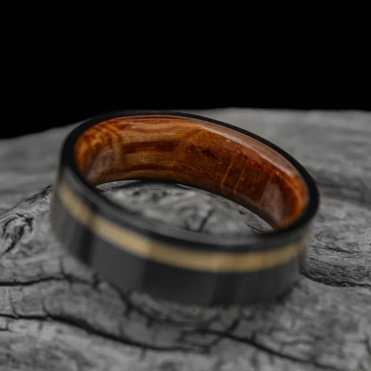 Black titanium wedding band with 10KY gold and whiskey barrel oak inlay, 7mm mens ring, unique design, free engraving, displayed on white sea branch.