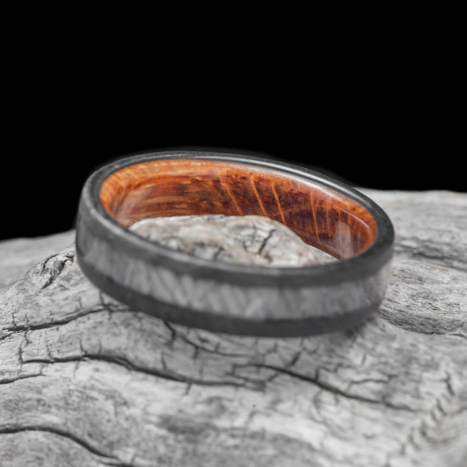 Mens wedding band with solid meteorite central inlay and whiskey barrel oak sleeve, 6mm unique forged ring, displayed on white sea branch, free engraving available.