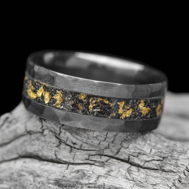 Black titanium mens wedding ring with central meteorite and gold leaf inlay, 8mm wide, displayed on a white sea branch, offering free engraving, unique design.
