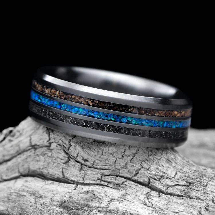 Black titanium ring with meteorite, crushed T-Rex bone, and blue opal central inlay, 7mm mens wedding band, unique design, free engraving, displayed on a white sea branch.