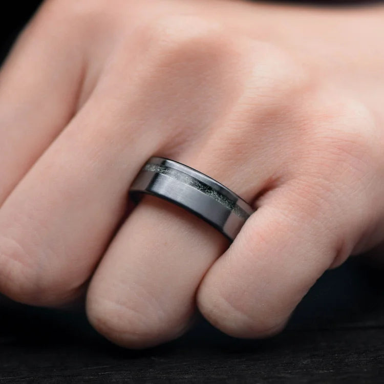 Hand wearing a Black Titanium Wedding Band featuring Moss Agate and Olivewood Inlay, 7mm width, unique mens wedding ring with free engraving option.