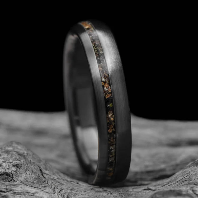 Black titanium wedding ring with crushed T-Rex inlay, brushed domed profile, 4mm custom band, unique simple design, free engraving, displayed on white sea branch.
