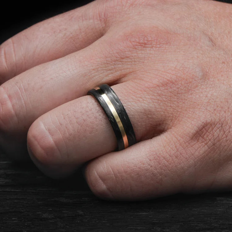 Mens 7mm forged wedding band with 10KY gold inlay and African blackwood inner sleeve, brushed flat profile, free engraving, shown on hand.