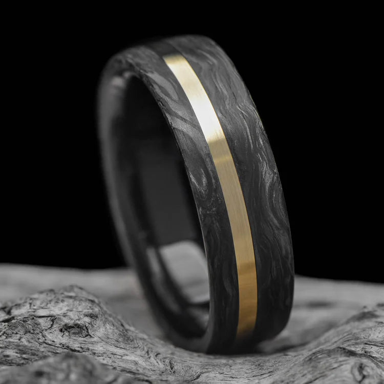 Forged mens wedding band with 10K yellow gold inlay and African blackwood inner sleeve, brushed flat profile, 7mm, displayed on white sea branch, free engraving available.