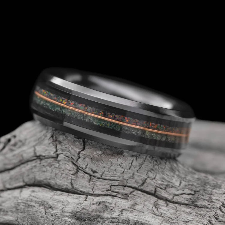 Black titanium wedding band with moss agate and black fire opal inlays, central forged guitar detail, 7mm mens ring, free engraving, displayed on a white sea branch.