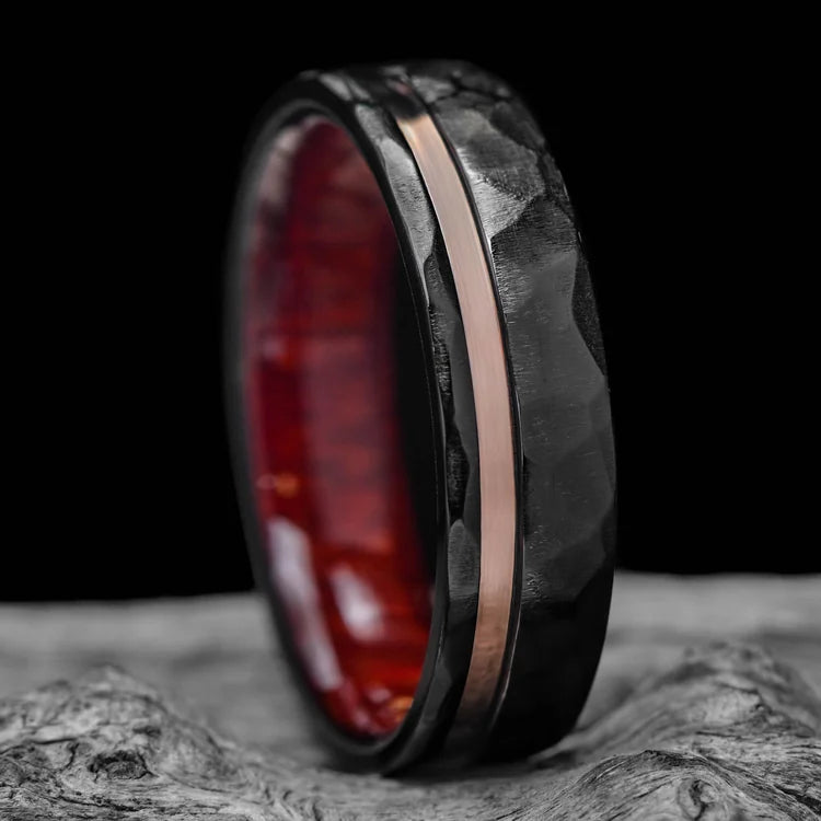 Black titanium mens wedding band with 14K rose gold inlay and bloodwood inner sleeve, featuring a faceted flat profile, displayed on a white sea branch, 7mm wide, free engraving available.