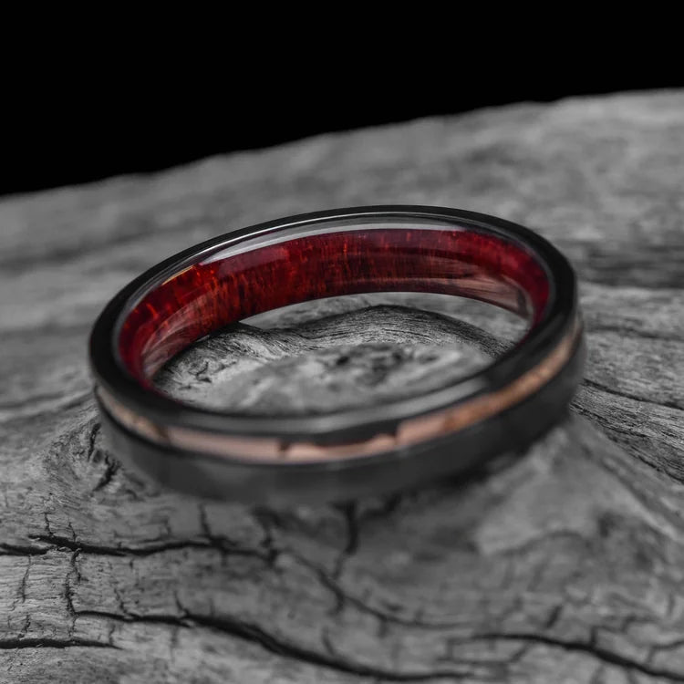 Black titanium wedding band with 14K rose gold and bloodwood inlay, featuring custom faceted flat design, displayed on a white sea branch, 4mm width, free engraving available, simple custom wedding ring.