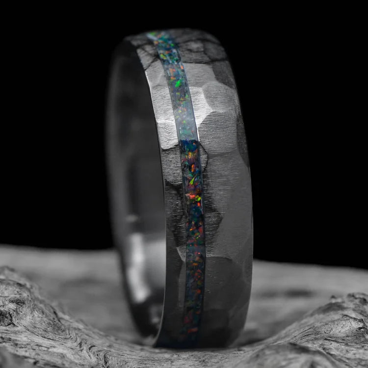 Black titanium mens wedding band with black fire opal inlay, faceted domed profile, 6mm width, unique design, free engraving, displayed on a white sea branch.