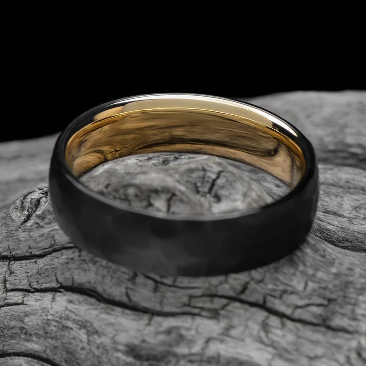 Black titanium wedding band with 14K yellow gold inner sleeve, faceted domed profile, 6mm mens ring, unique design, free engraving, displayed on white sea branch.