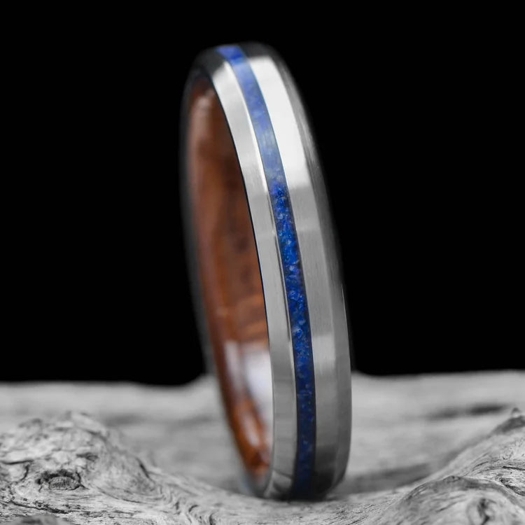 Titanium wedding band with lapis lazuli inlay and whiskey barrel oak sleeve, featuring brushed bevel profile, 4mm custom simple ring, displayed on white sea branch. Free engraving available.