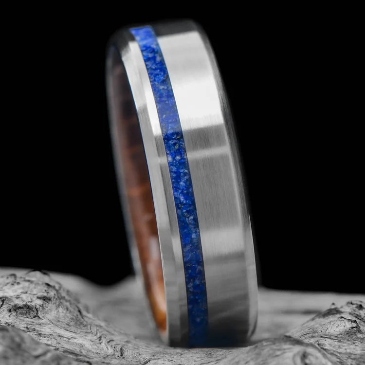 Titanium wedding band with lapis lazuli inlay and whiskey barrel oak sleeve, 7mm mens ring, unique design, free engraving, displayed on a white sea branch.