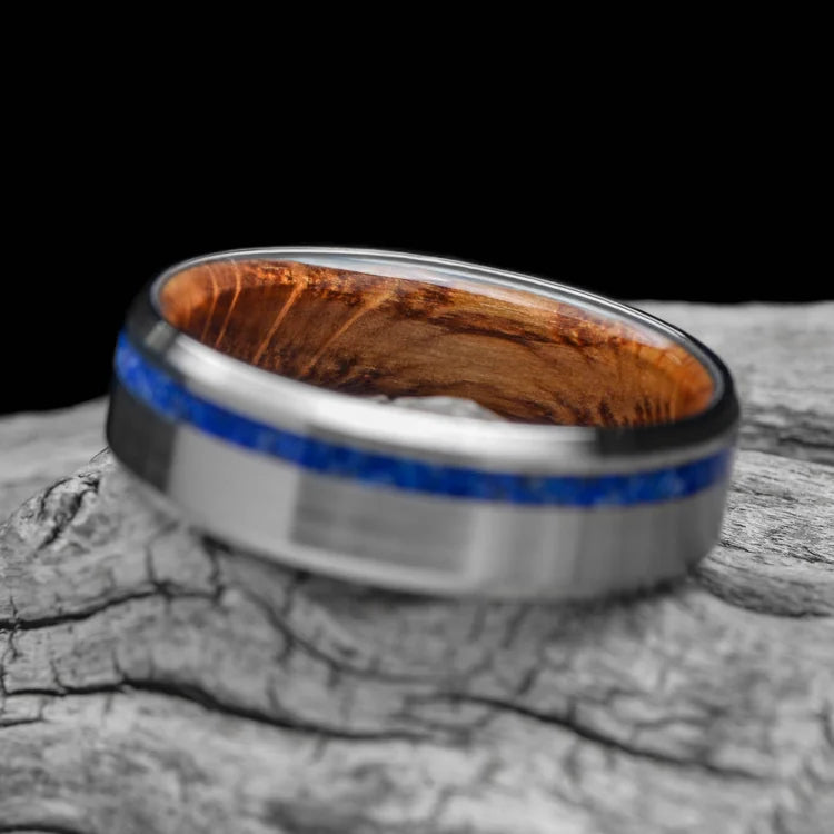 Titanium wedding band with lapis lazuli inlay and whiskey barrel oak sleeve, 7mm mens ring, unique design, free engraving, displayed on a white sea branch.
