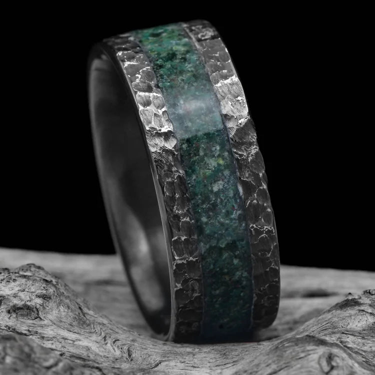 Black titanium mens wedding band with central moss agate inlay, unique hammered flat profile, 8mm width, displayed on white sea branch, free engraving available.