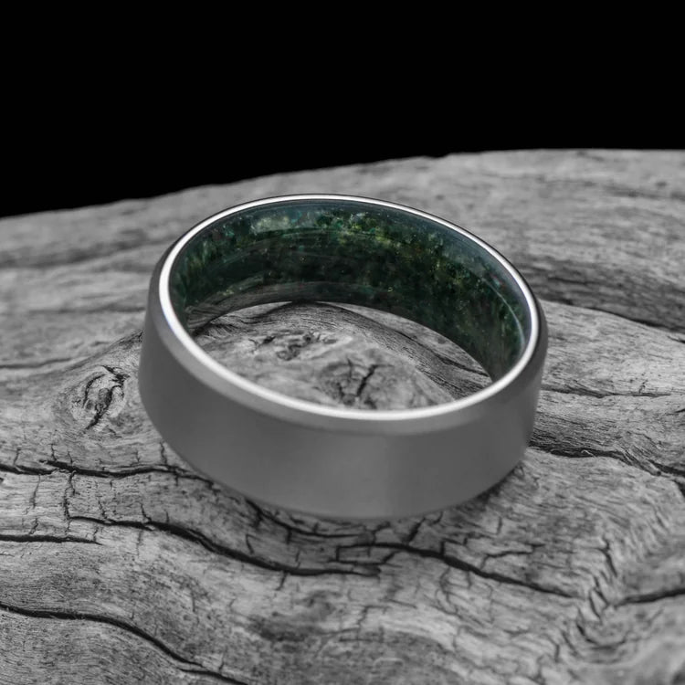 Titanium wedding band with moss agate inner sleeve, sandblasted bevel profile, 8mm mens ring, unique design, free engraving, displayed on white sea branch.