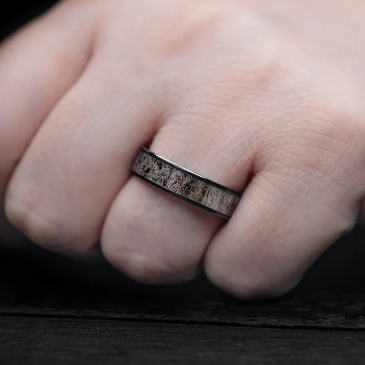 Black titanium ring with central deer antler inlay on a hand, showcasing a polished flat profile, 6mm mens wedding band, unique design, free engraving option.