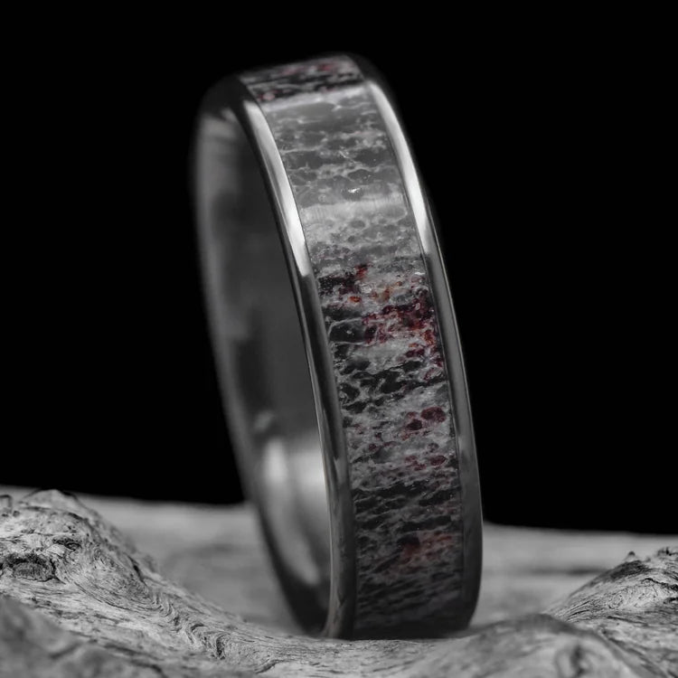 Black titanium mens wedding ring with central deer antler inlay, 6mm wide, polished flat design, unique and customizable with free engraving, displayed on a white sea branch.
