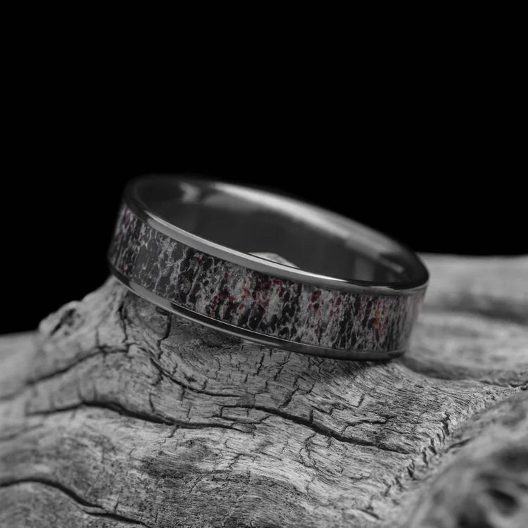 Black titanium ring with central deer antler inlay, 6mm mens wedding band, polished flat profile, unique design, free engraving, displayed on a white sea branch.