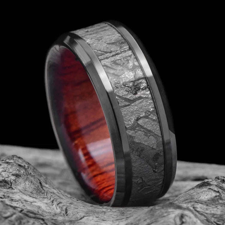 Black titanium ring featuring a central meteorite inlay and bloodwood inner sleeve, 8mm mens wedding band with free engraving, unique design on white background.