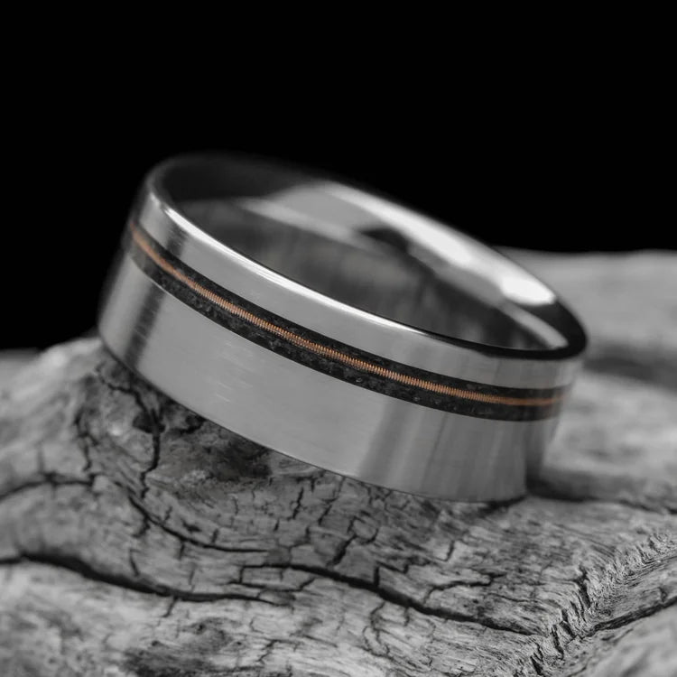 Titanium wedding band with black onyx and guitar string inlay, featuring free engraving, 8mm width, mens brushed flat profile, unique design, displayed on a white sea branch.