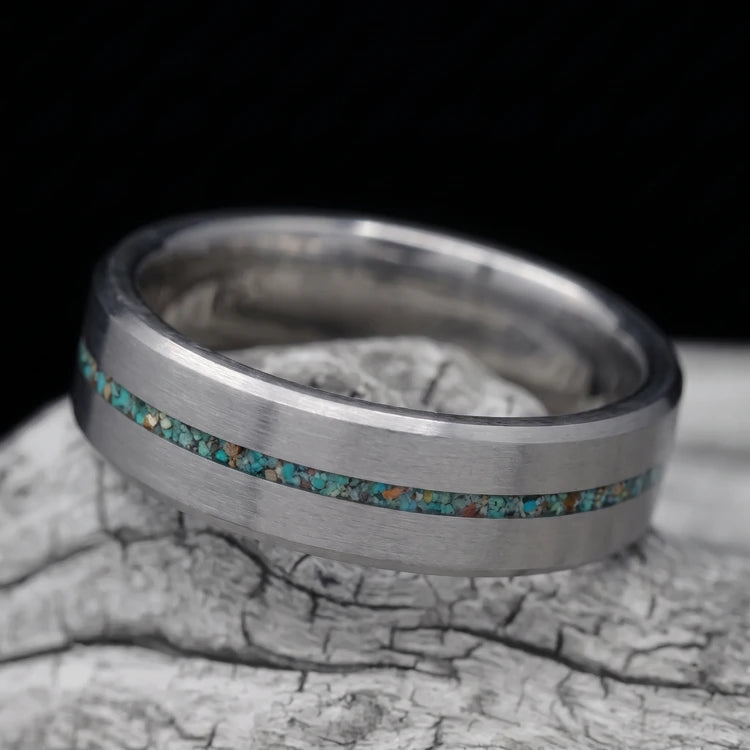 8mm brushed tantalum men’s wedding band with central turquoise inlay and beveled edges, resting on a white sea branch