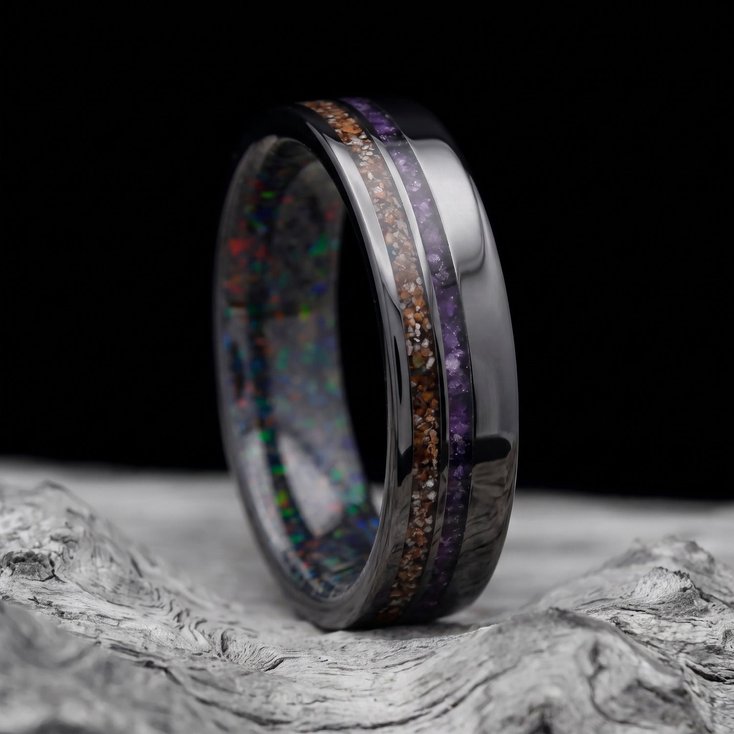 Black titanium men’s wedding band with crushed T-Rex and amethyst inlays and a black fire opal inner sleeve, resting on a white sea branch.