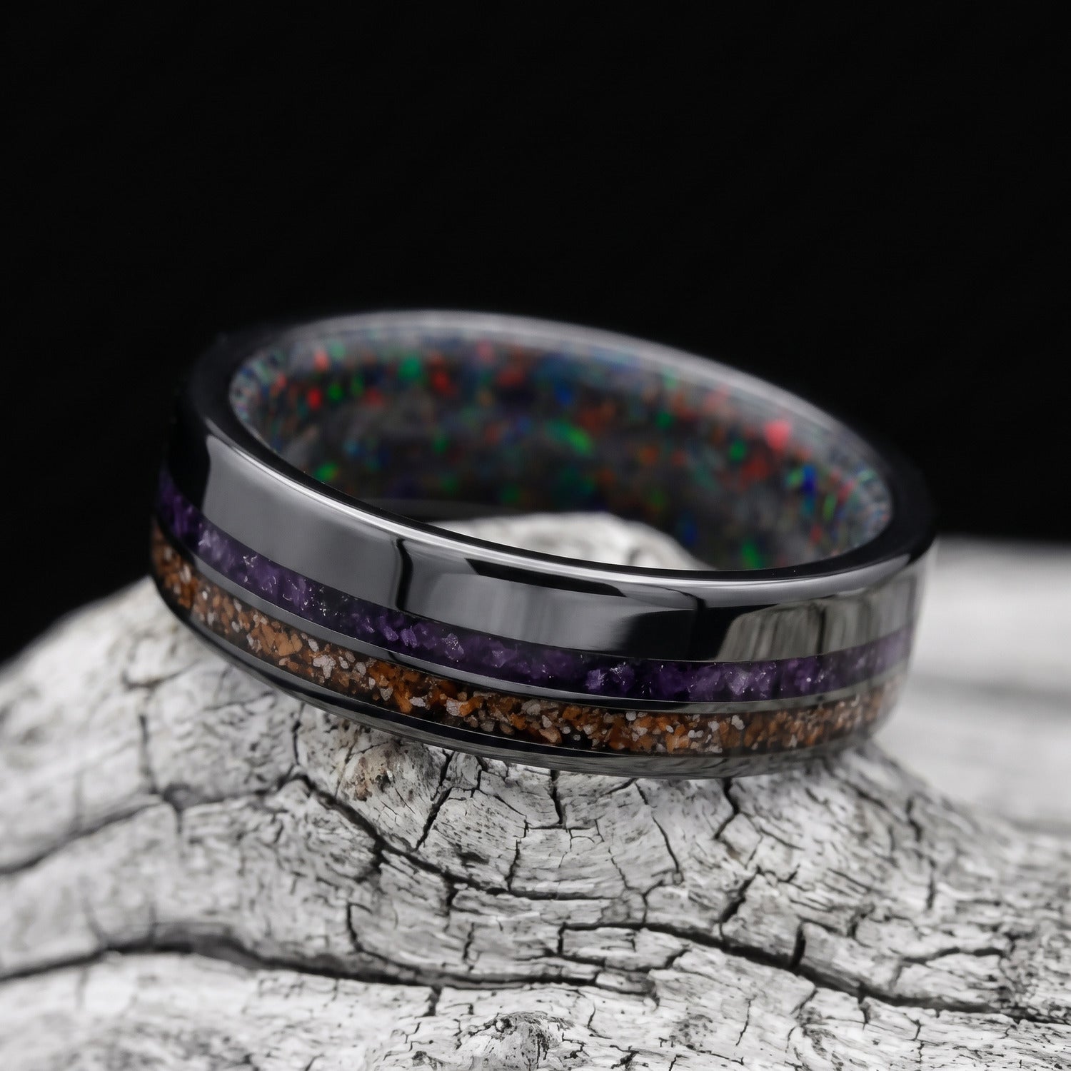 Black titanium mens wedding band with crushed T-Rex and amethyst inlays and a black fire opal inner sleeve, resting on a white sea branch.