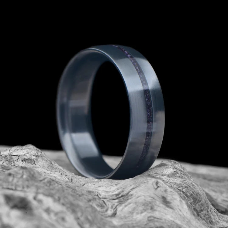 Zirconium men's wedding band with central amethyst inlay, brushed domed profile, 7mm, laying on a white sea branch.