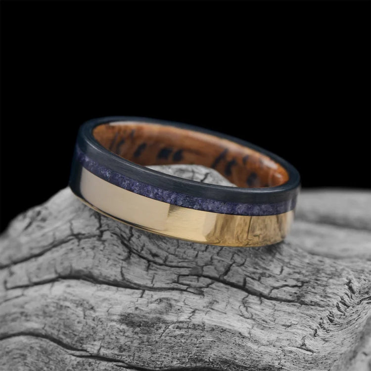 18K yellow gold men's wedding band with unidirectional and amethyst inlays, featuring a whiskey barrel oak inner sleeve, shown on a white sea branch, 6mm width, free engraving available.