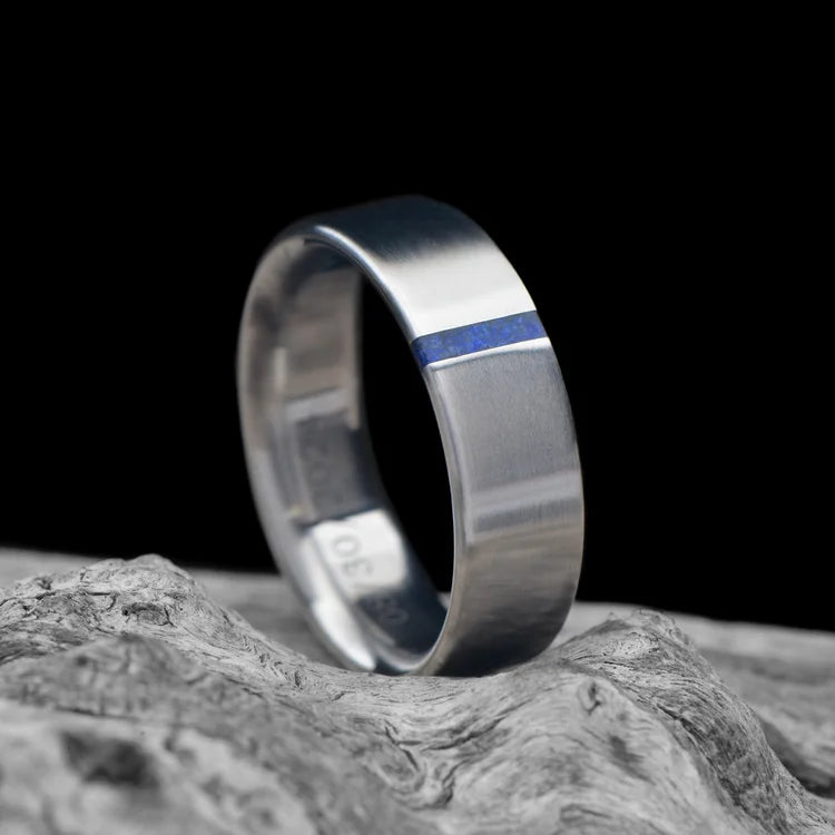 Titanium wedding band with lapis lazuli inlay, 6mm brushed flat profile, men's custom ring on white sea branch.