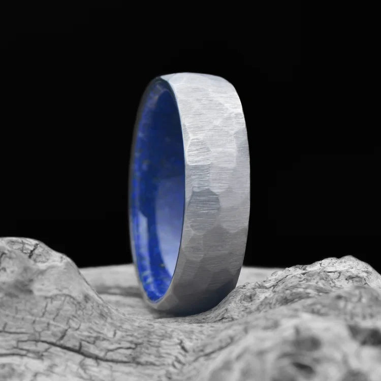 Faceted titanium men's wedding band with lapis lazuli inner sleeve, 7mm unique domed design, free engraving, displayed on white sea branch.