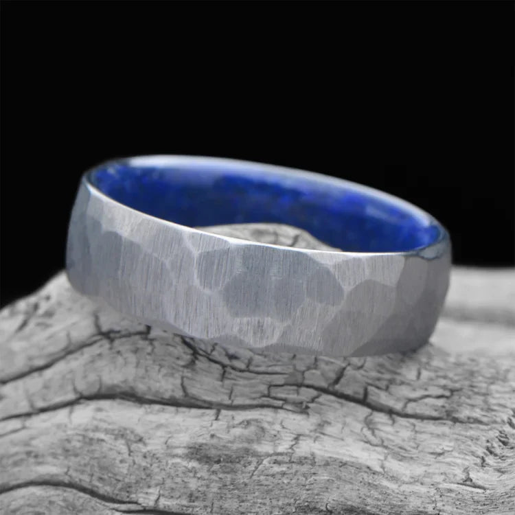 Faceted titanium ring with lapis lazuli inner sleeve, 7mm men's wedding band, unique domed design, displayed on a white sea branch.