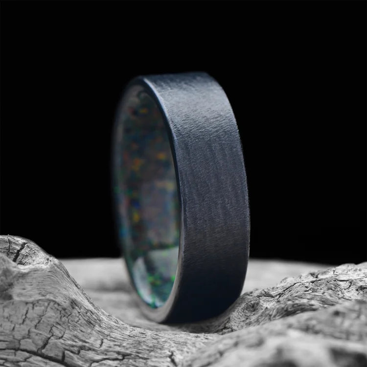 Black Titanium Wedding Band with Black Fire Opal Inner Sleeve, 7mm Men's Wedding Ring, Unique Granite Finish, displayed on white sea branch, free engraving available.