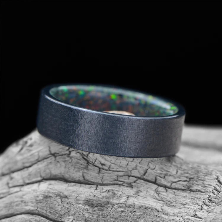 Black Titanium Wedding Band with Black Fire Opal Inner Sleeve, 7mm Men's Wedding Ring, Unique Granite Finish, displayed on a white sea branch, free engraving available.